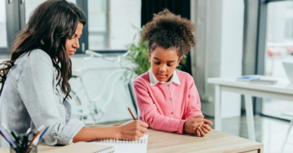 How to home school starting today Black mom and elementary age student daughter sitting at kitchen table doing school work