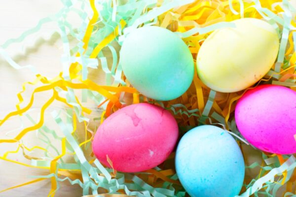 Easy egg coloring ideas (DIY Spring Kids Activities) with a group of coloring dyed Easter eggs sitting on paper Easter grass on a table
