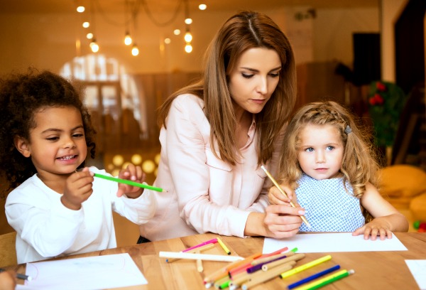 african american child and caucasian child doing worksheets at a table with a caucasian female teacher