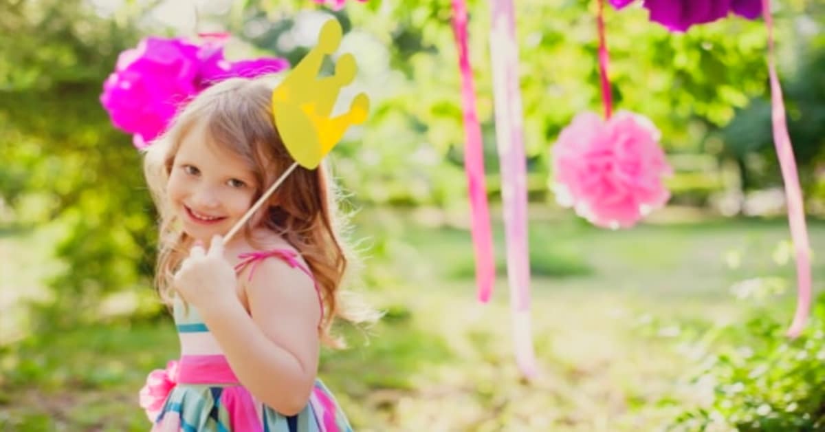 Make Up Your Own Holiday Day Ideas for Kids young smiling girl looking into camera holding crown and flower photo props at an outdoor holiday party