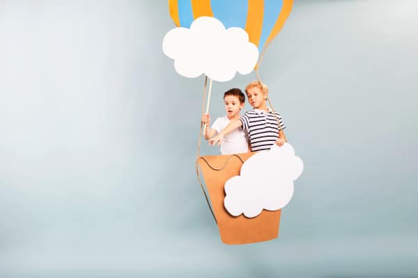 How To Start Unschooling two caucasian boys in a hot air balloon made of paper and holding paper clouds