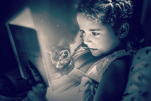 Summer Reading Programs for Free Stuff black and white picture of a little girl reading a book in bed with a kitten sitting on her and looking at the book