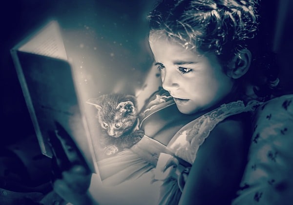 Summer Reading Programs for Kids for Free Stuff black and white picture of a little girl reading a book in bed with a kitten sitting on her and looking at the book