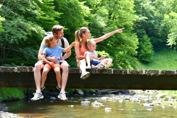 national parks with family sitting on a wood bridge over a creek pointing at something in the trees