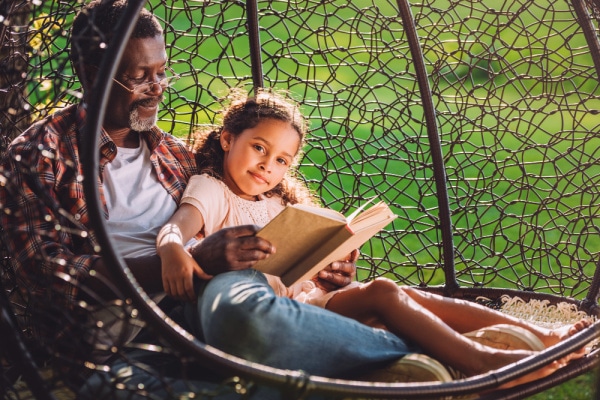 african american grandpa sitting on a swing with an black elementary age girl and reading a book together for Homeschool Without Internet