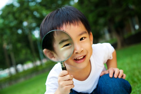 What Is Unschooling cute asian boy looking through a magnifying glass outside