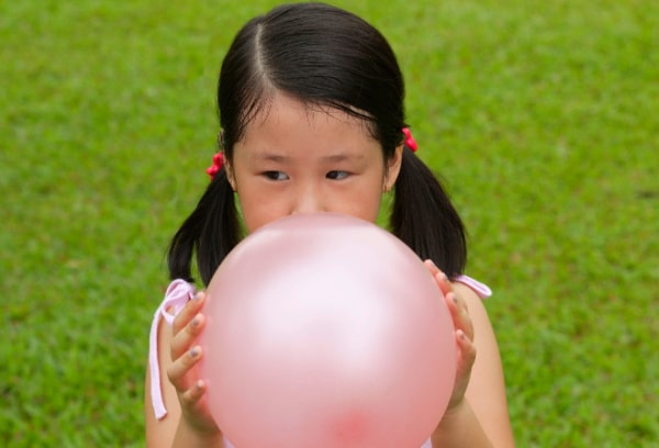 Autism awareness for kids young girl with dark ponytails blowing up a balloons on green grass