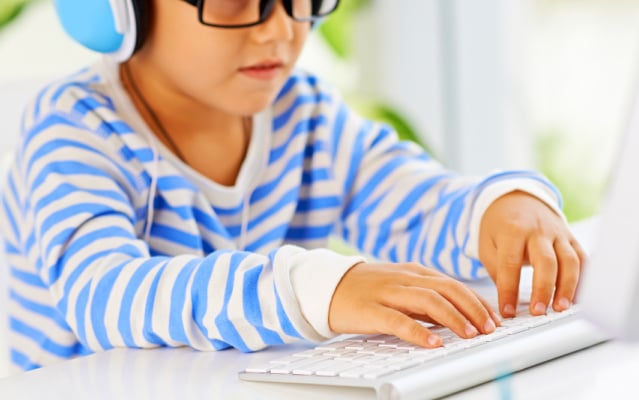 boy with glasses wearing headphones typing on a keyboard while Hybrid Schooling