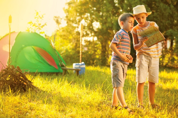 Camping As A Family two kids looking at a map with a family camping tent behind them