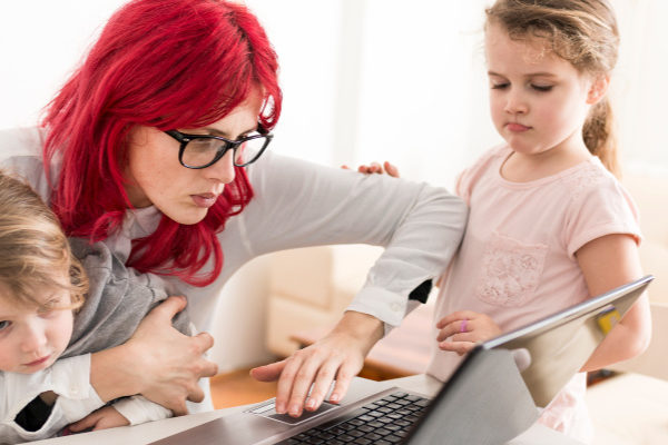 School At Home: Why You Hate Homeschooling mom with bright red dyed hair looking at laptop while trying to deal with two preschoolers