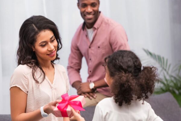 best gifts for homeschool moms young girl handing her homeschool mom gift with dad smiling in background