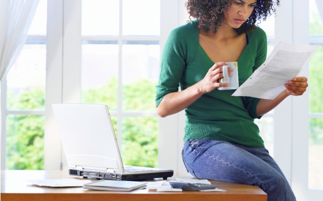 african american mom sitting on a desk and looking confused over a homeschool transcript