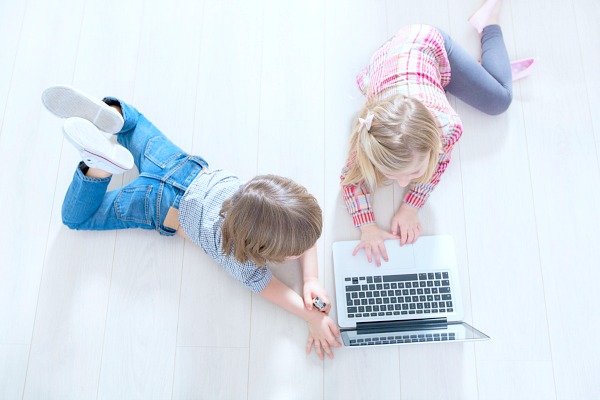 how to start homeschooling TODAY looking down on a little boy and girl lying on their stomachs on a white floor and playing with a laptop