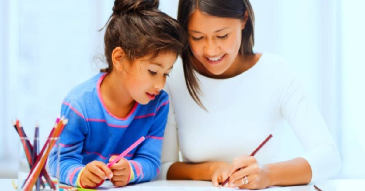 Starting homeschool mid year: smiling mother working on homeschooling with young daughter at a table