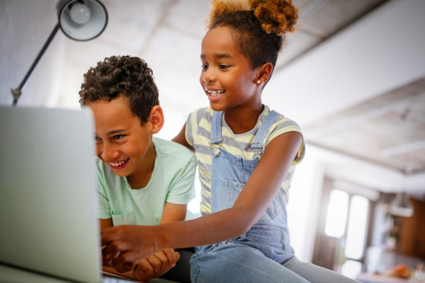 elementary age black girl and boy laughing in front of a laptop while doing a Virtual Scavenger Hunt for Kids
