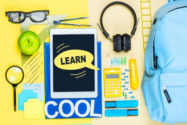 Supplies Needed for Homeschooling: school supplies like paper glasses magnifying glass tablet calculator backpack sitting on a yellow table