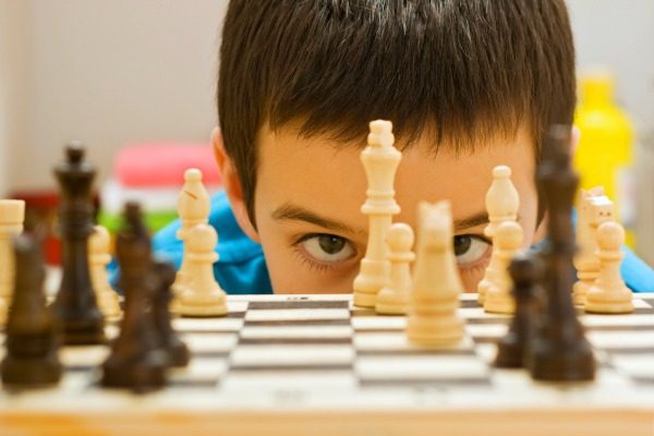 Gameschooling homeschool close up of boy's eyes looking through chess pawns into the camera