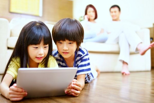 a boy and girl laying on floor and looking at iPad