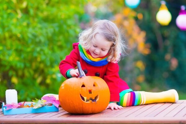 preschool activities for Halloween little girl sitting on a table outside looking at a jackolantern