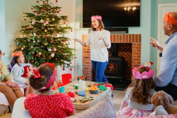 Best Family Games For The Holidays with family in living room in front of Christmas tree playing charades