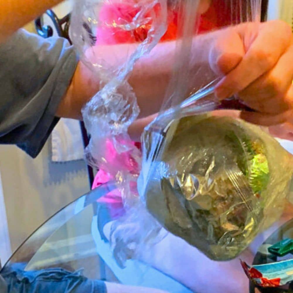 Saran Wrap Ball Game How To Make It And Play It (Teen Prize Ideas) - teenagers playing unwrap ball game around a table and unwrapping the plastic wrap ball