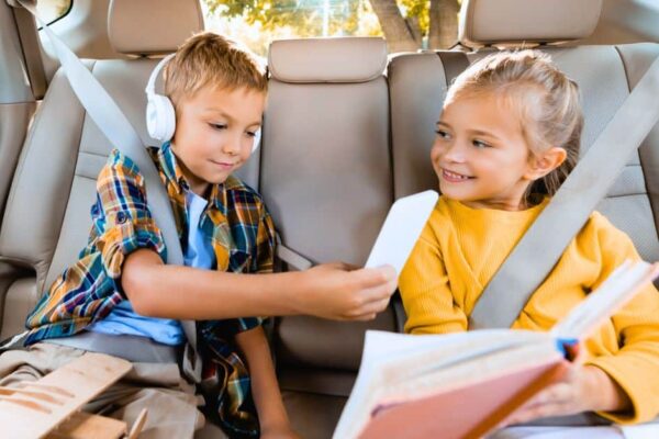 Road Trip Boredom Busters for Kids - two kids in backseat on a long car trip reading and playing with phone